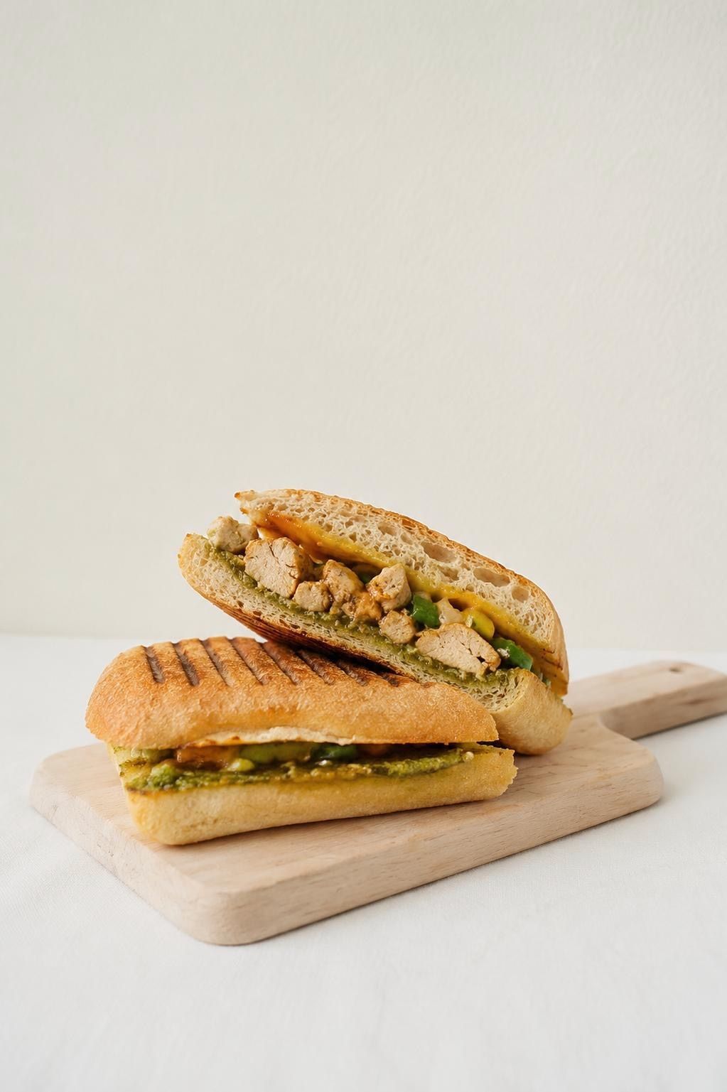 A chicken panini, pressed and halved on a wooden board